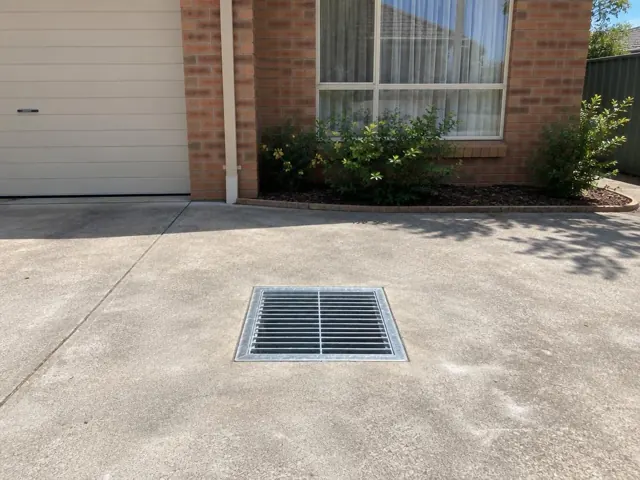 Driveway drain grate set in concrete beside a brick house and garage in Marayong