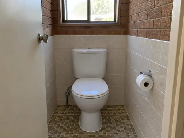 Clean white toilet in a tiled bathroom with brick walls and a small window in Quakers Hill