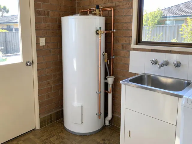 Hot water cylinder with copper pipework beside a laundry sink and tiled wall in Doonside